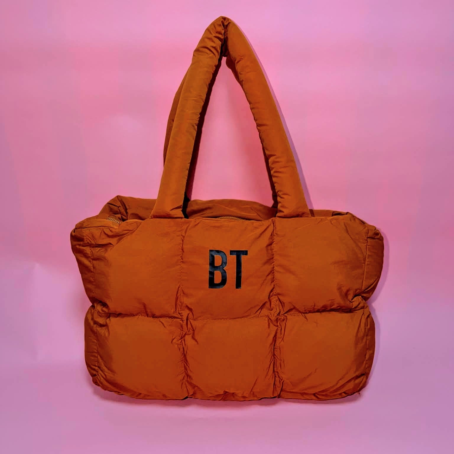 Orange puffer bag with 'BT' initials on a pink gradient background