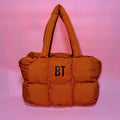 Orange puffer bag with 'BT' initials on a pink gradient background