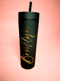 Black tumbler with gold text on a pink gradient background