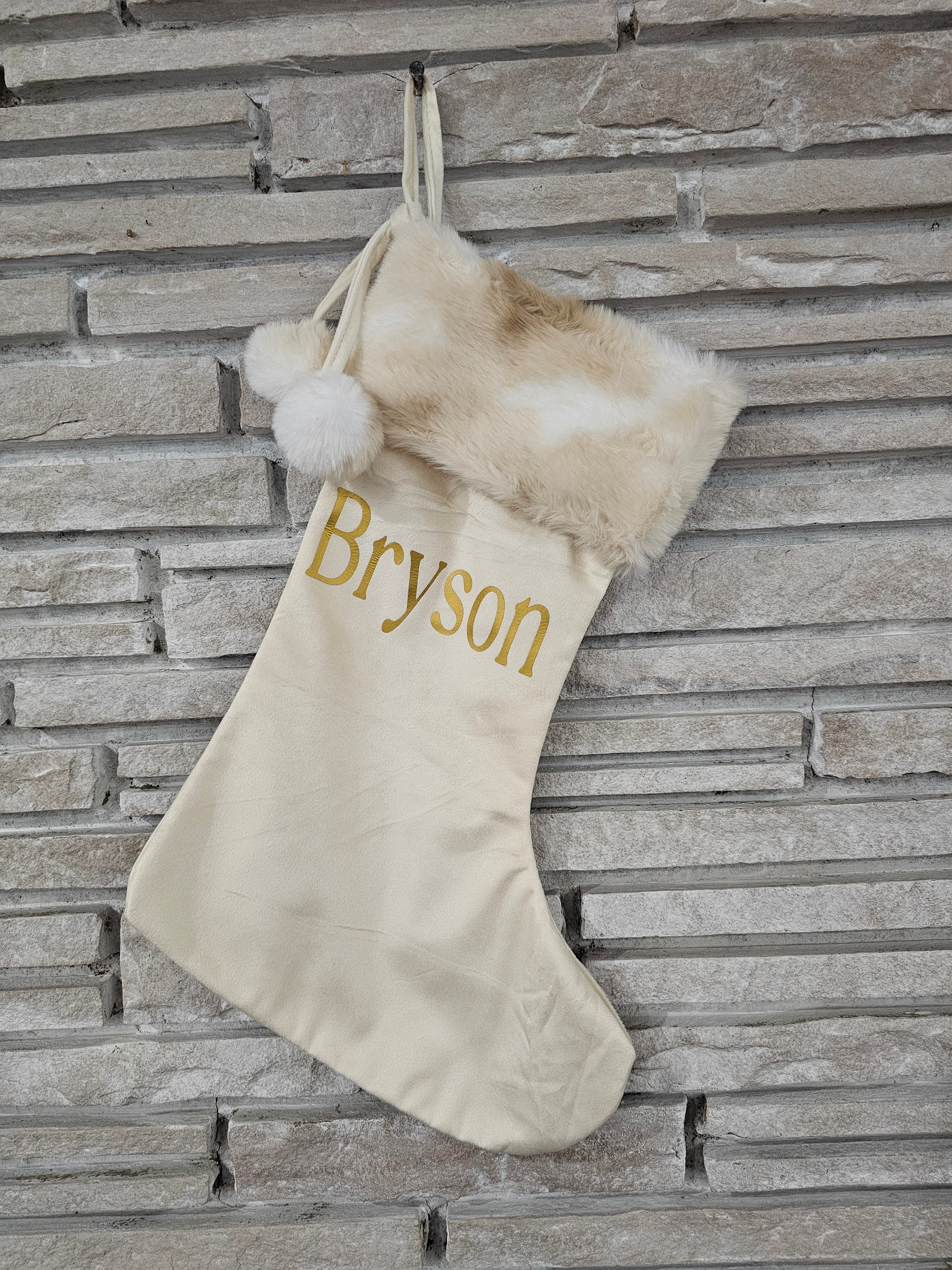 Ivory holiday stocking with cozy faux fur top, pom balls, and custom gold HTV vinyl name applied by hand