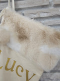 High-quality ivory holiday stocking with tan and white faux fur top, pom balls, and custom metallic gold HTV vinyl name