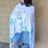 Person wearing a white blanket with blue snowflake patterns against a beige brick wall.