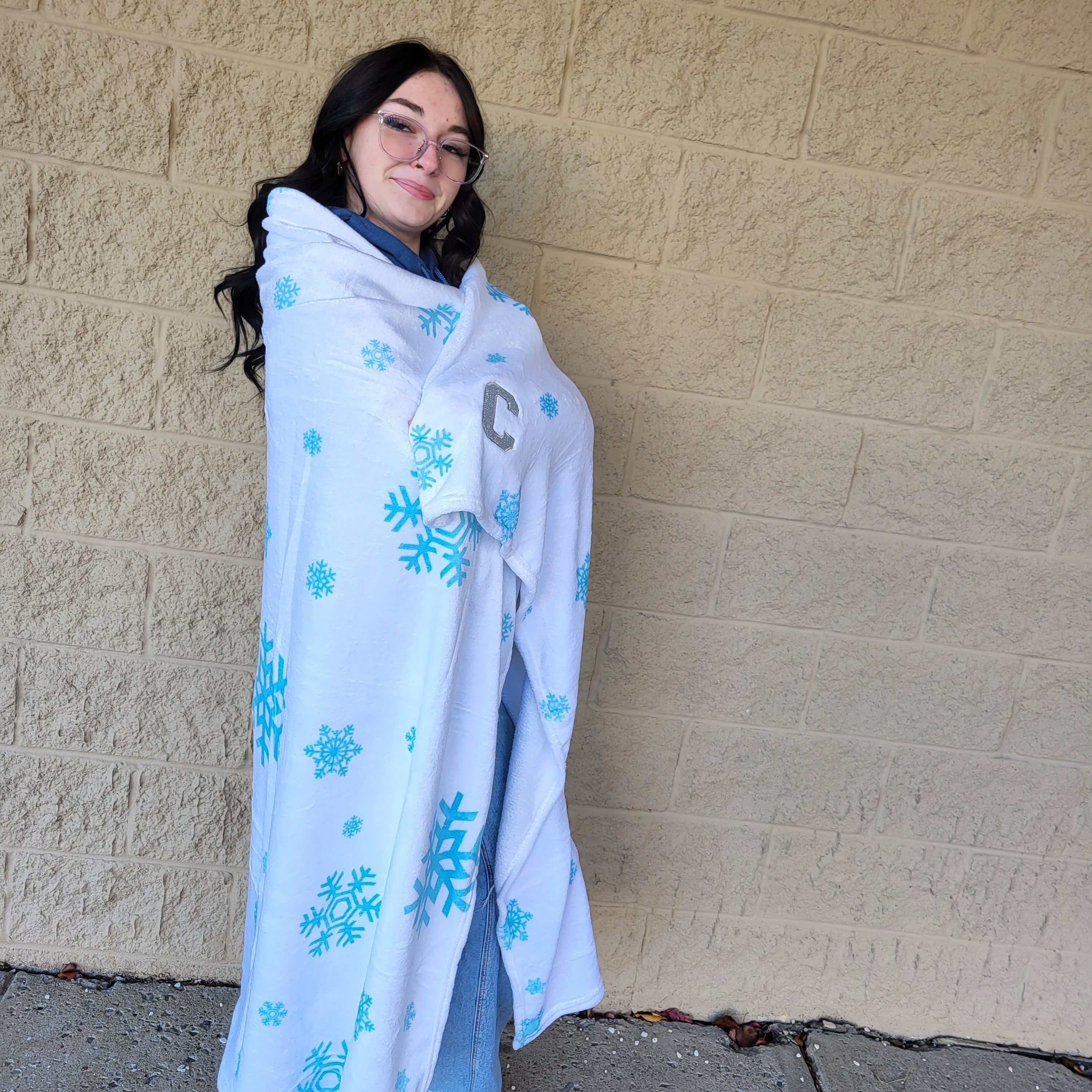 Person wrapped in a blanket with snowflake patterns against a beige wall.