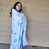 Person wrapped in a blanket with snowflake patterns against a beige wall.