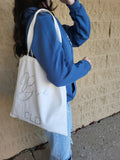 Person holding a white tote bag with 'Bride' and 'CLB' text against a beige wall.