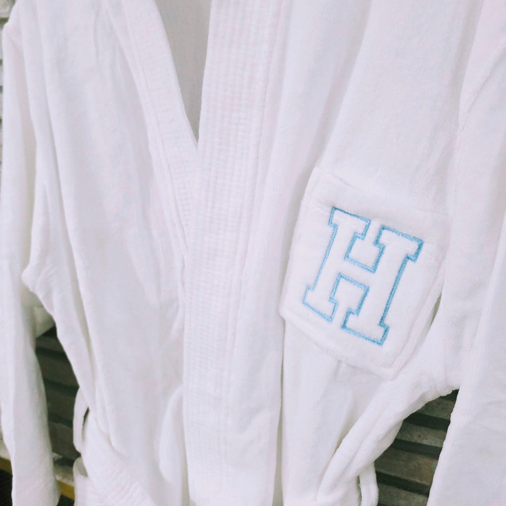 White robe with a blue 'H' monogram on a wooden surface
