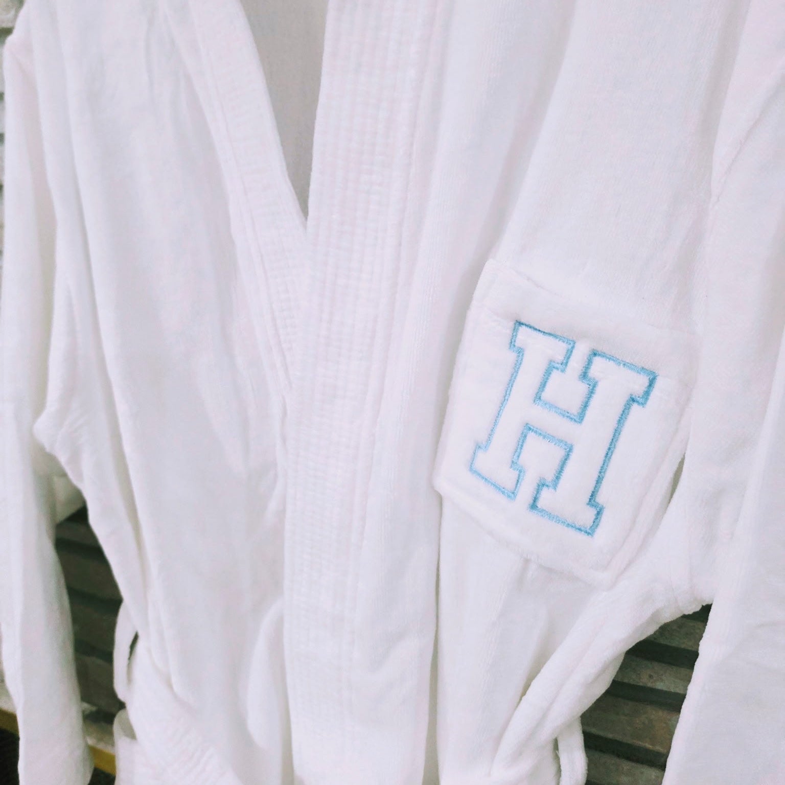 White robe with a blue 'H' monogram on a wooden surface