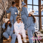 Five women modeling matching ski-themed loungewear in a rustic indoor setting with large windows showing a snowy mountain view. The outfits include light blue and white hoodies and sweatpants sets with 'APRES SKI' and mountain graphics.