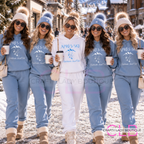 Five women walking outdoors in a snowy village setting, wearing matching ski-themed loungewear. Four women wear light blue hoodies and joggers with white mountain graphics and 'APRÈS-SKI' text, while the center woman wears a white matching set.