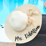 Beige sun hat with a bow and 'Mrs. Robertson' text by a pool.