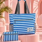 A blue and white striped tote bag with dark gray handles and side mesh pockets, displayed alongside a matching zip pouch on pink display pedestals in a pastel pink studio setting.