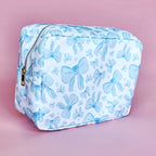 White makeup bag with an all-over light blue bow pattern, featuring a rectangular shape and zippered closure — perfect for brides and travel use.