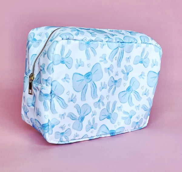 White makeup bag with an all-over light blue bow pattern, featuring a rectangular shape and zippered closure — perfect for brides and travel use.