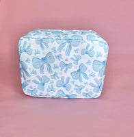 White makeup bag with an all-over light blue bow pattern, featuring a rectangular shape and zippered closure — perfect for brides and travel use.