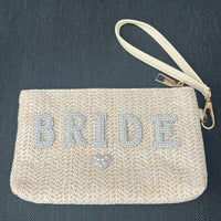 Beige clutch bag with 'BRIDE' in rhinestones on a dark background