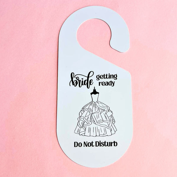 Two double-sided bridal door hangers with black designs. One reads “Bride Getting Ready – Do Not Disturb” with a wedding dress illustration, the other reads “Honeymooners – Please Do Not Disturb” with wedding rings and a bow.