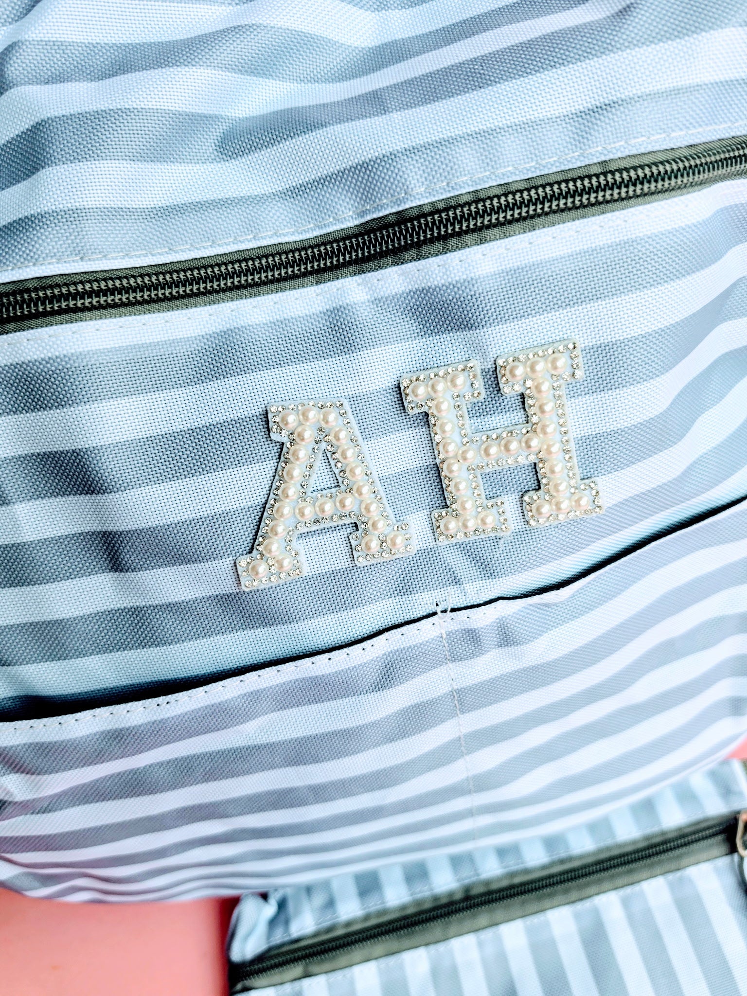 Grey and white striped oversized beach tote bag with pearl patch monogram initials and matching zip wristlet on a pink background.