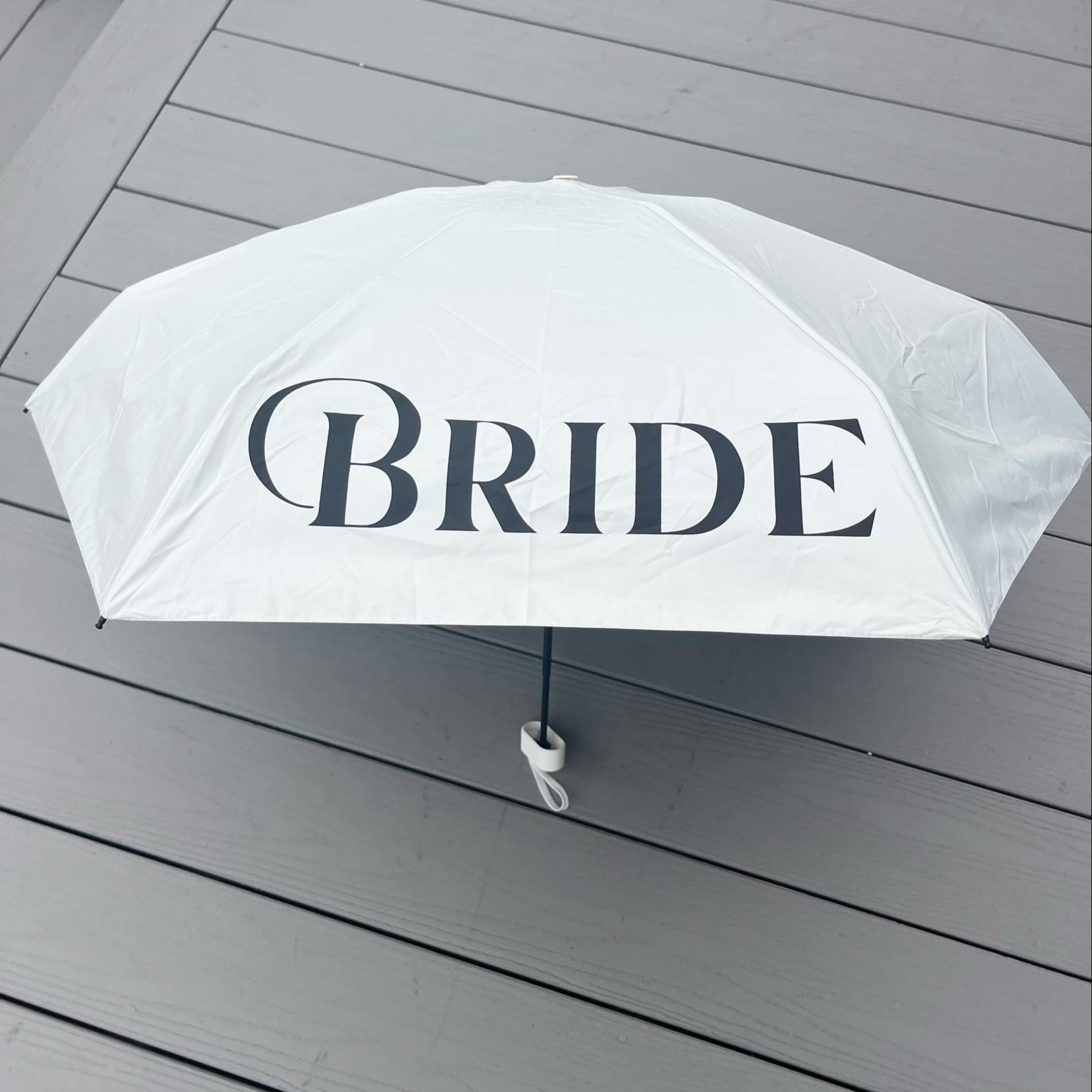 White umbrella with 'BRIDE' text on a wooden surface