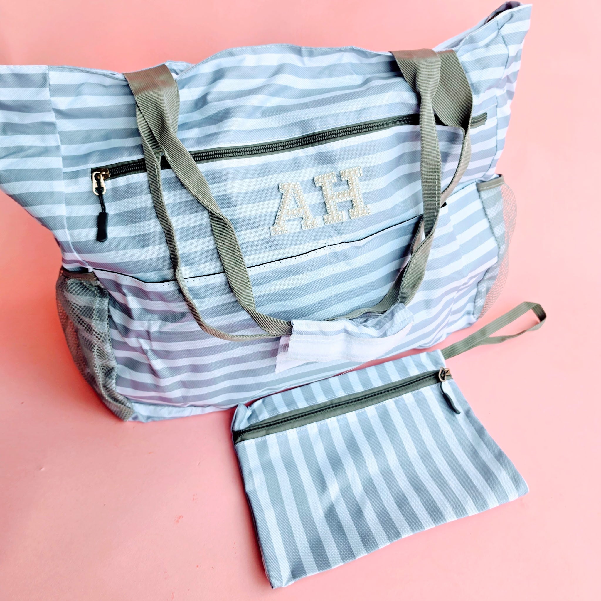 Grey and white striped oversized beach tote bag with pearl patch monogram initials and matching zip wristlet on a pink background.