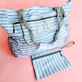 Grey and white striped oversized beach tote bag with pearl patch monogram initials and matching zip wristlet on a pink background.