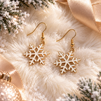 A pair of gold-tone and white snowflake dangle earrings displayed on a fluffy cream faux fur surface with holiday decorations, including pine branches, a gold ribbon, and a glittering ornament.