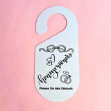 Two double-sided bridal door hangers with black designs. One reads “Bride Getting Ready – Do Not Disturb” with a wedding dress illustration, the other reads “Honeymooners – Please Do Not Disturb” with wedding rings and a bow.