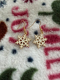 Gold snowflake drop earrings displayed on a cozy winter blanket background.
