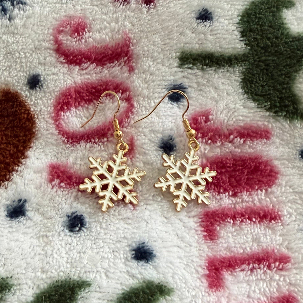 Gold snowflake drop earrings displayed on a cozy winter blanket background.
