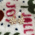 Gold snowflake drop earrings displayed on a cozy winter blanket background.
