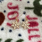 Gold snowflake drop earrings displayed on a cozy winter blanket background.
