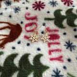 Gold snowflake drop earrings displayed on a cozy winter blanket background.

