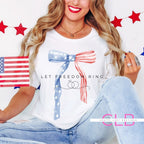 Woman wearing a white t-shirt with a red, white, and blue watercolor bow design, holding a small American flag, styled for a patriotic celebration.