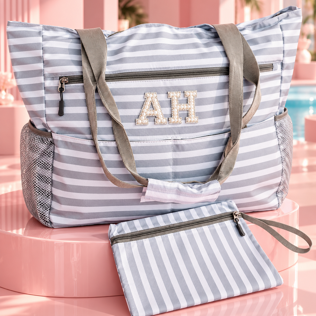 A striped tote bag with gray shoulder straps and a matching zip pouch, displayed on a pink pedestal in a stylized poolside setting. The bag features a light blue and white stripe pattern, gray mesh side pockets, and a monogrammed 'AH' on the front.