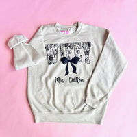 Beige personalized Wifey sweatshirt with black bow and custom last name text, cozy bride and wife gift, perfect for weddings, honeymoons, or newlyweds