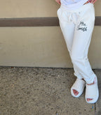 Person wearing white sweatpants with 'Mrs. Smith' printed on the side, standing against a beige wall.