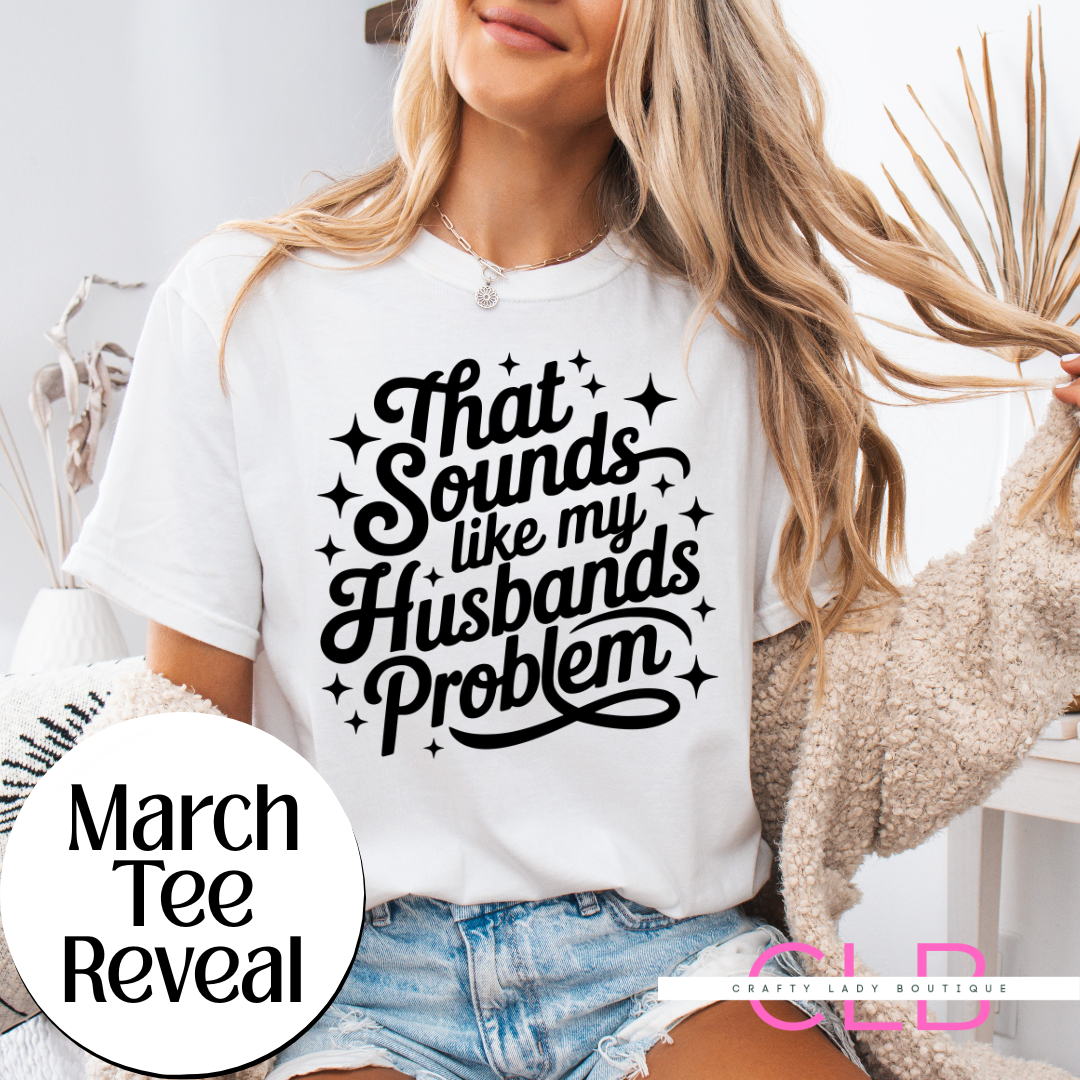 White t-shirt with black script text reading “That Sounds Like My Husband’s Problem” worn by woman with casual outfit.