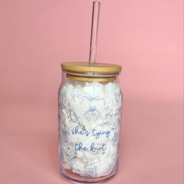 Clear glass cup with bamboo lid and straw featuring blue “She’s Tying the Knot” text and wedding doodles, perfect for brides and iced coffee lovers.
