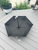 Black umbrella on a wooden deck with plants in the background