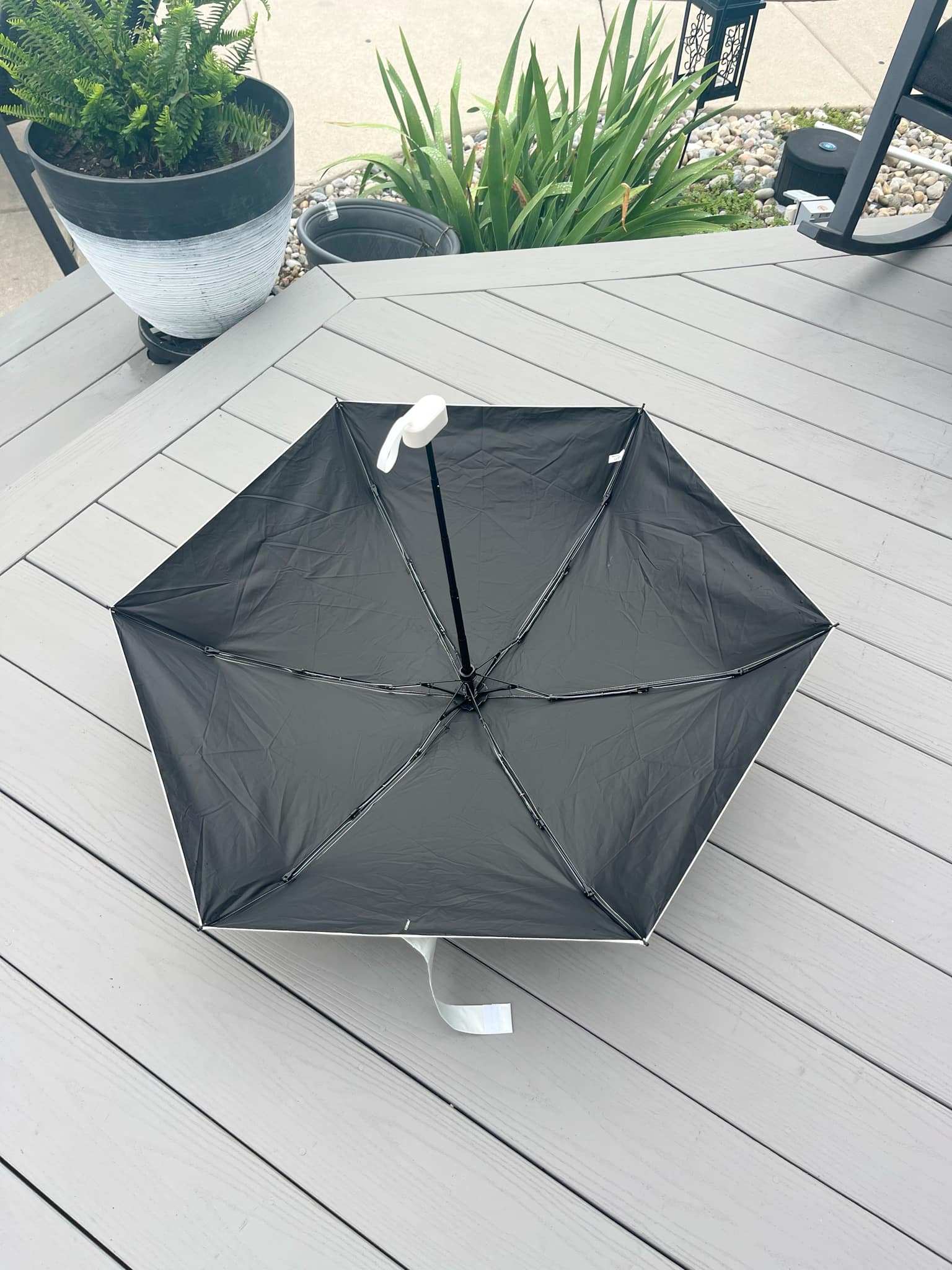 Black umbrella on a wooden deck with plants in the background