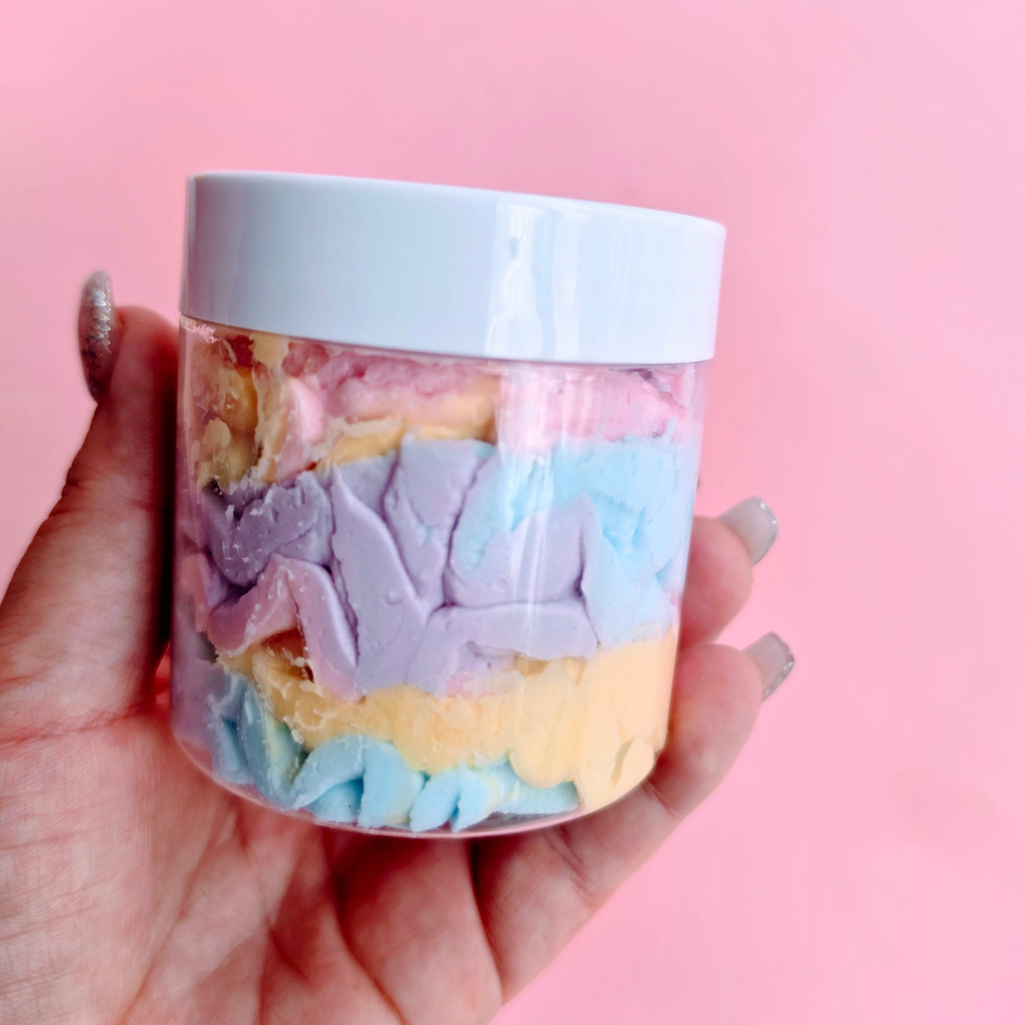 Hand holding a jar of colorful bath bombs against a pink background