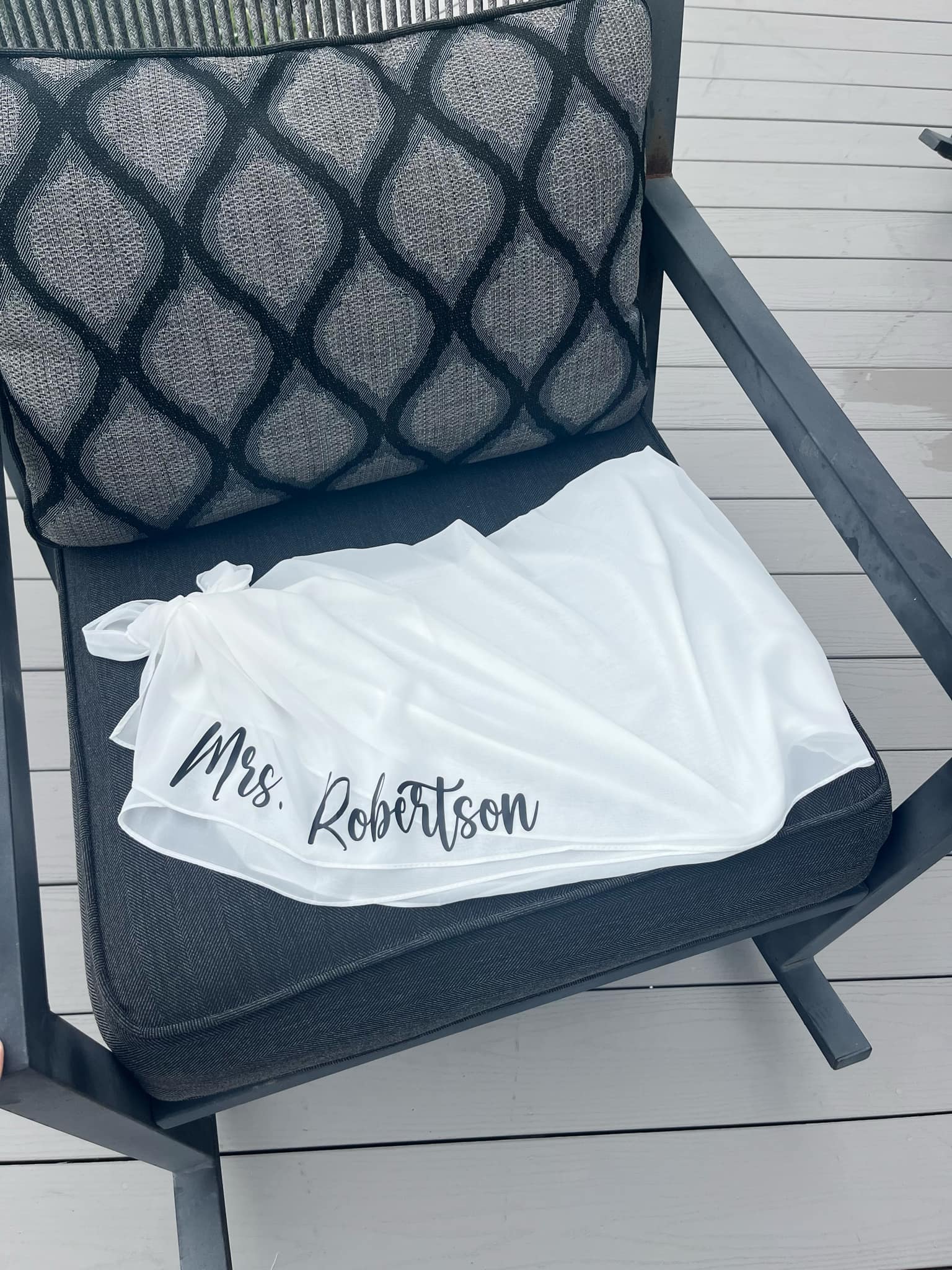 White Sarong with 'Mrs. Robertson' printed on it, draped over a chair on a wooden deck.