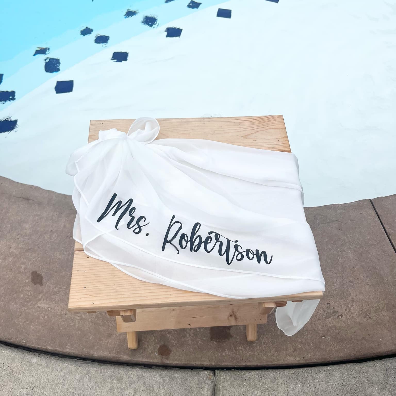 White Sarong with 'Mrs. Robertson' printed on it, draped over a wooden stool against a blue and white patterned background.