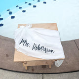 White Sarong with 'Mrs. Robertson' printed on it, draped over a wooden stool against a blue and white patterned background.