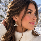 A woman in a white knit turtleneck sweater wearing a silver snowflake dangle earring, photographed outdoors in a snowy landscape.