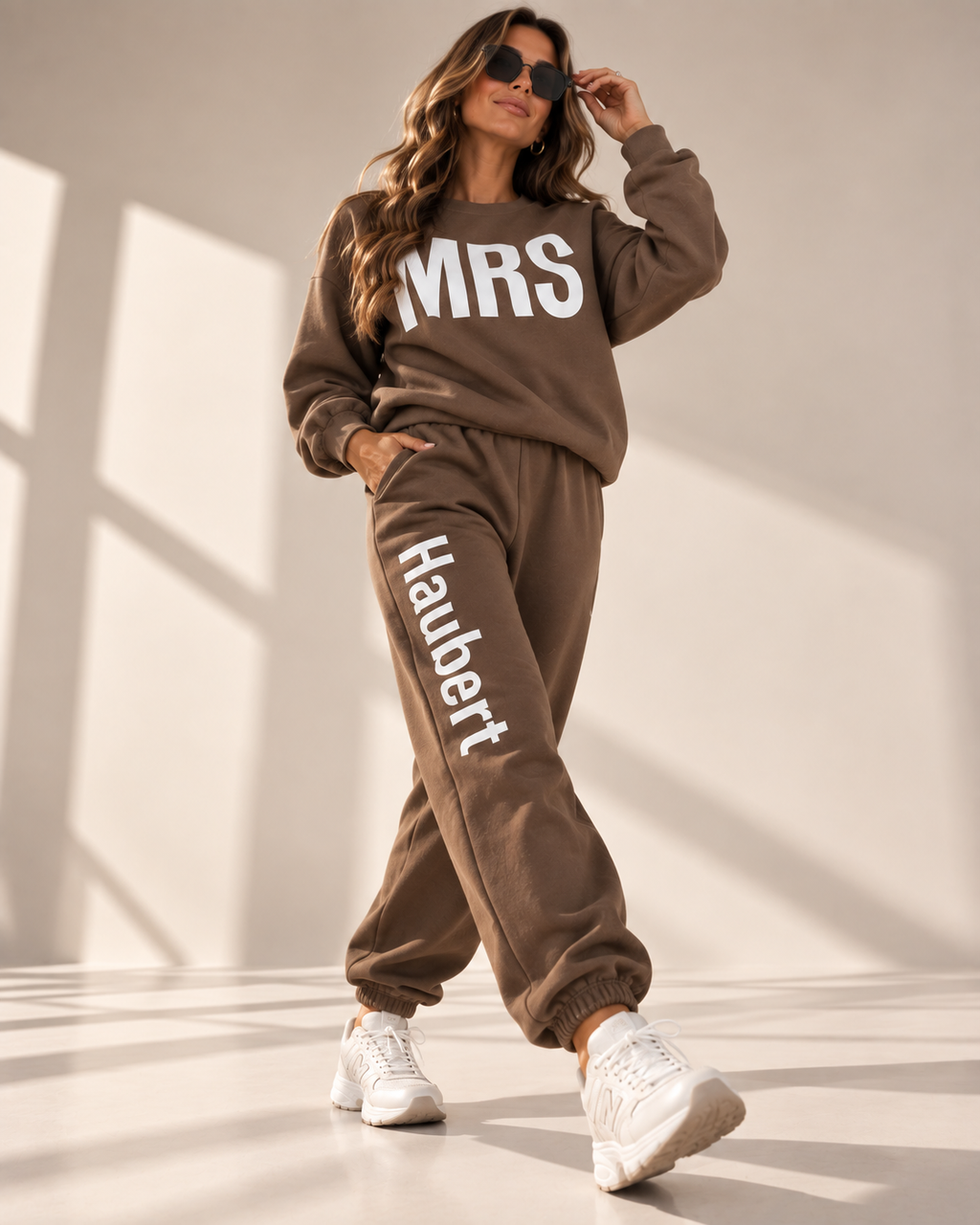 A woman models a matching brown sweatshirt and jogger pants set with white text. The sweatshirt features 'MRS' across the chest, and the joggers feature 'Haubert' down the left leg.