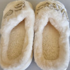 Pair of white fuzzy slippers with decorative elements on a light gray background