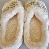 Pair of white fuzzy slippers with decorative elements on a light gray background